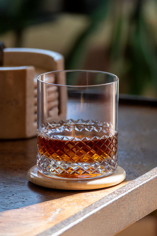 Glass of whiskey on a wooden coaster with blurred background