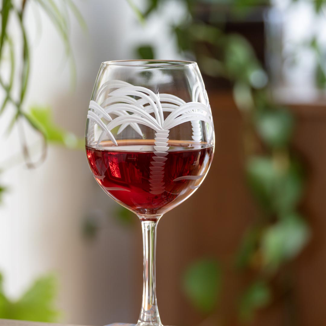 Rolf Glass Palm Tree 18oz Red Wine Balloon Glass full of red wine on a desk