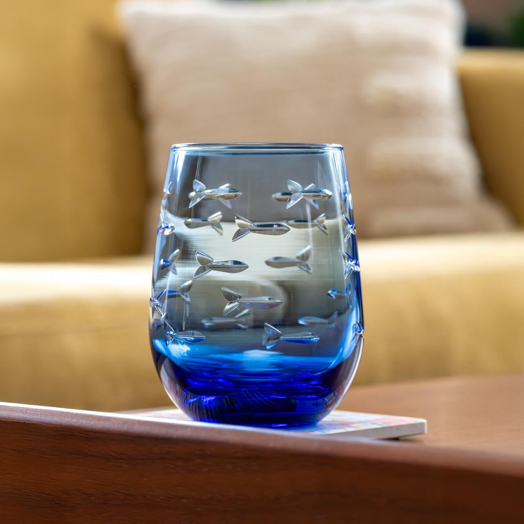 Rolf Glass School of Fish 15oz Blue Stemless Wine Glass on a coffee table