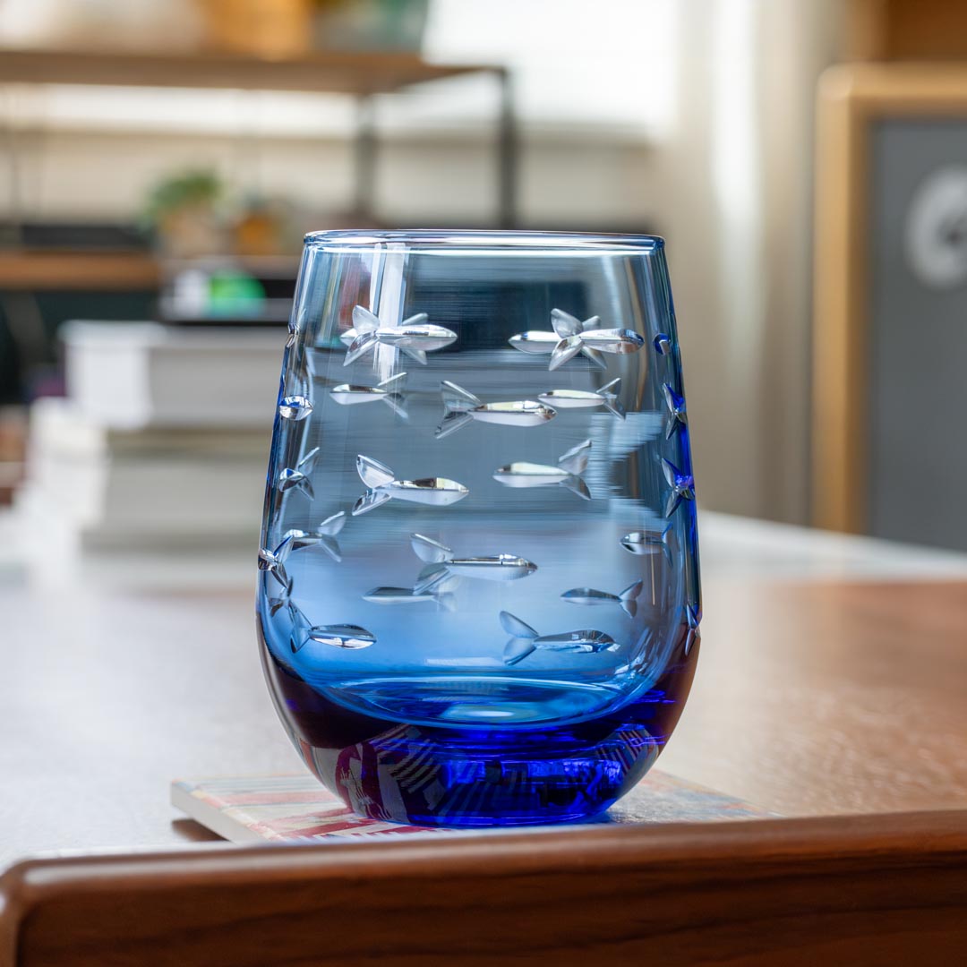 Rolf Glass School of Fish 15oz Blue Stemless Wine Glass on a coffee table