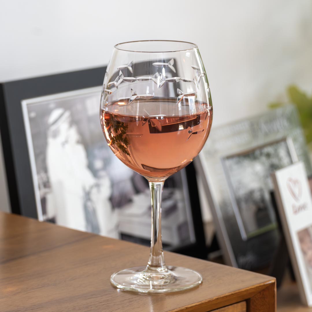 Rolf Glass School of Fish 18oz Balloon Red Wine Glass on a wood desk with photos in the background