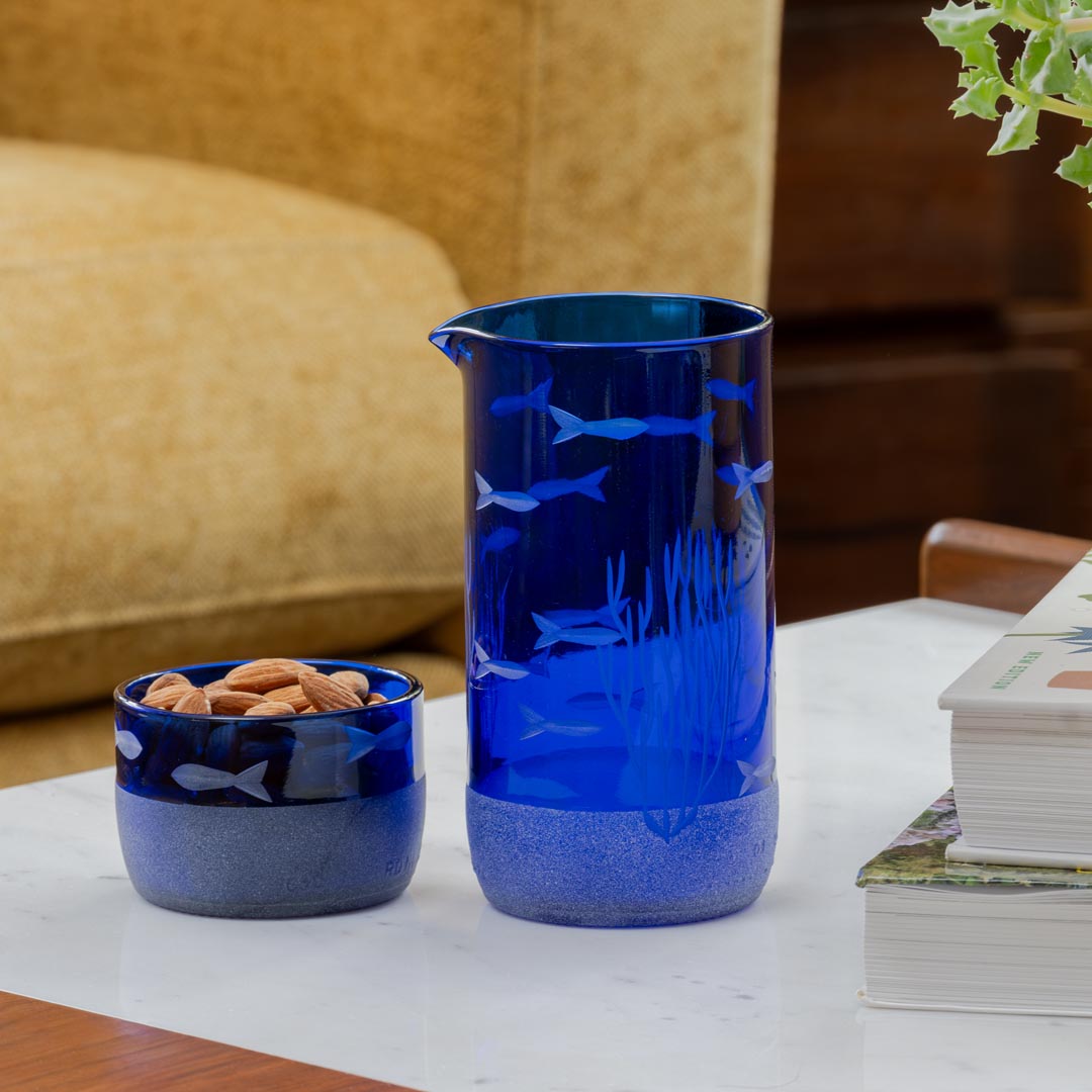 Rolf Glass School of Fish Twice Around Blue 13oz Pitcher and 2 Inch Mini Sipper Giftbox Set on a coffee table