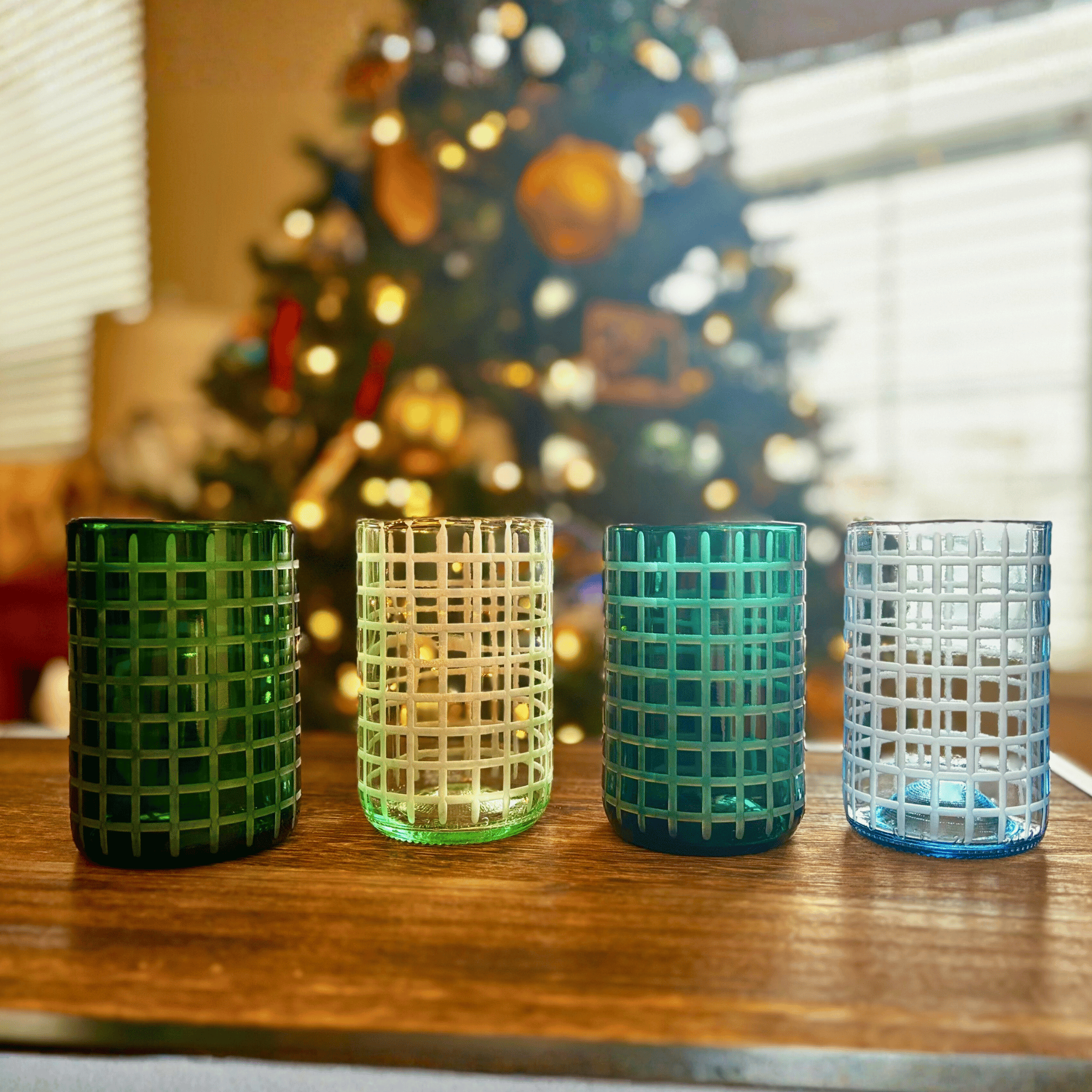 Four textured glass tumblers on a wooden surface with a blurred Christmas tree in the background.