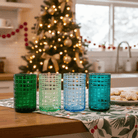 Four colorful textured glasses on a table with a Christmas tree in the background